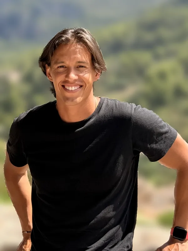 Juan Sebastián Vaca smiling, with a wooded hillside behind him